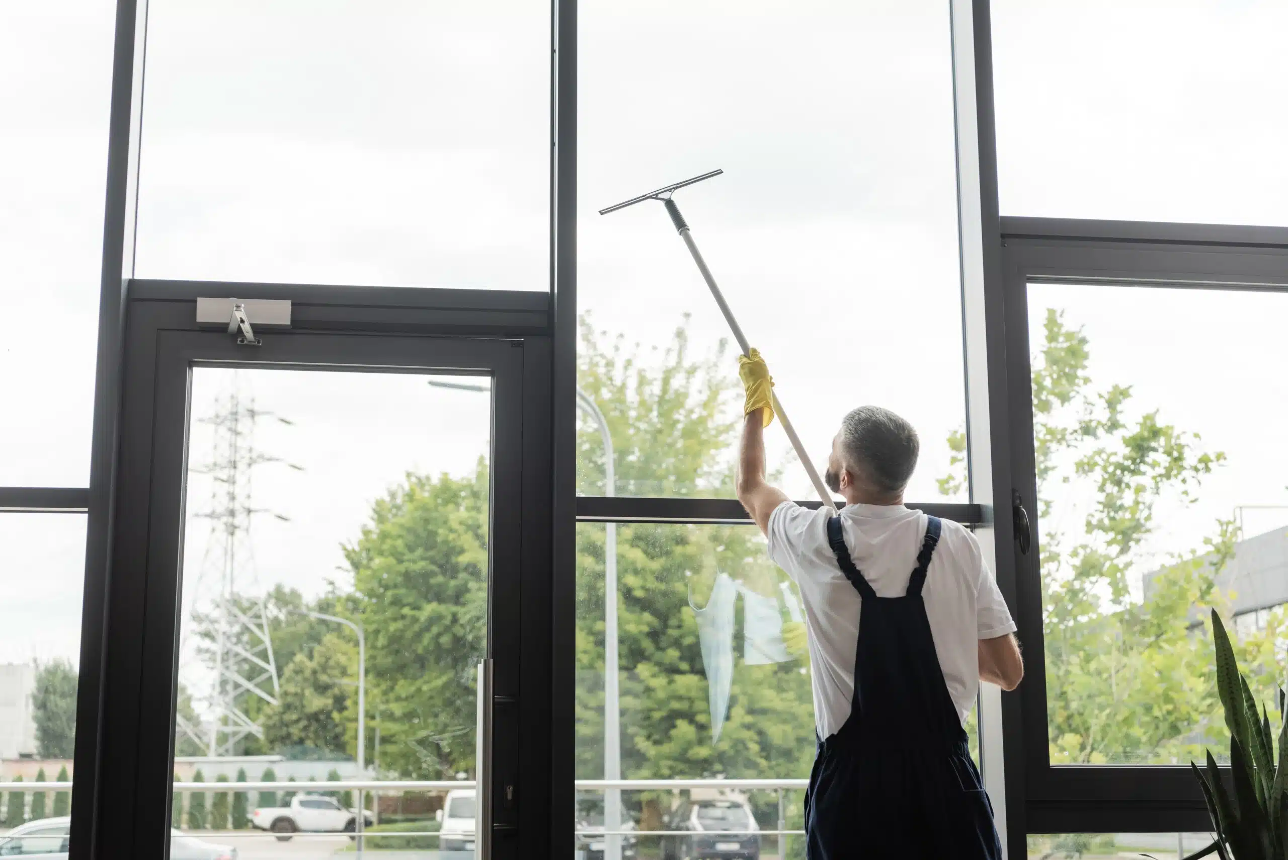 Back,View,Of,Man,In,Overalls,Washing,Large,Office,Windows